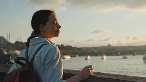 A young girl with a backpack looking at the Bosphorus from the bridge at sunset