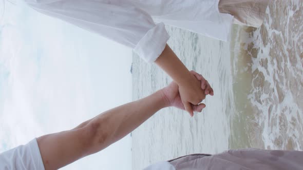 Vertical Video: Attractive Asian couple enjoying romantic sunset on the beach and holding hands.