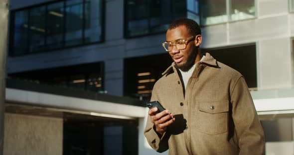 AfricanAmerican Man is Typing on a Mobile Phone While Walking in the City