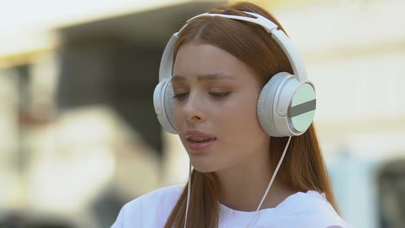 Crying Female Teen Getting Sentimental Listening to Music in Headphones Outdoors