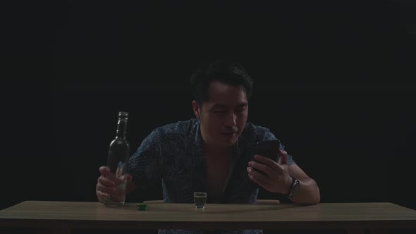 Asian Man Pouring Vodka In A Shot Glass Before Drinking During Having Video Call In Black Background