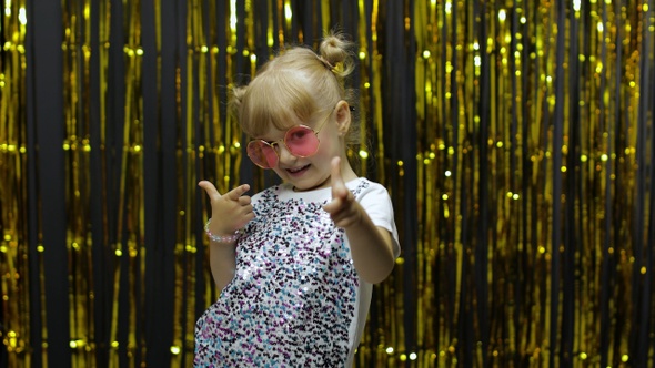 Child Dancing, Pointing Fingers at Camera. Girl Posing on Background with Foil Golden Curtain