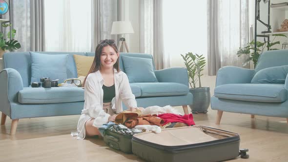 Young Woman Packing Clothes In Suitcase And Warmly Smile To Camera At Home, Preparing For Vacation