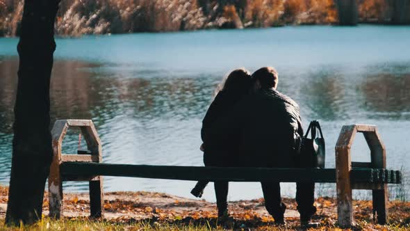 Young Romantic Couple Sitting on a Bench in an Autumn Park By the River