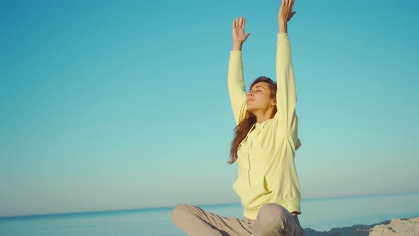 Beautiful Calm Brunette Woman in Yellow Hoodie Meditating and Doing Yoga Practice on Beautiful Calm