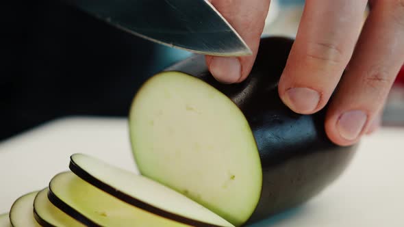 Close-up: A chef cuts an eggplant with fine pressure on a cutting surface in a professional kitchen