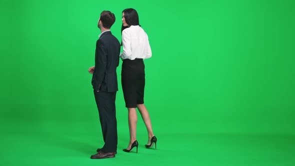 Couple of Young People in Suits Man and Woman Stand in the Green Space of the Chromakey Watching and