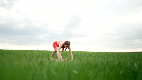 Sporty Woman in Orange Wear Doing Yoga in Fresh Green Field