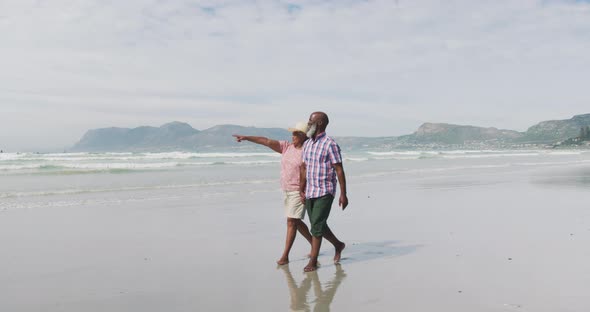 Mixed race senior couple walking and holding hands at the beach