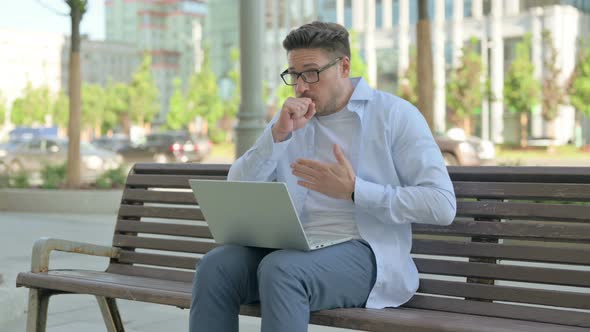 Coughing Man Using Laptop While Sitting Outdoor on Bench