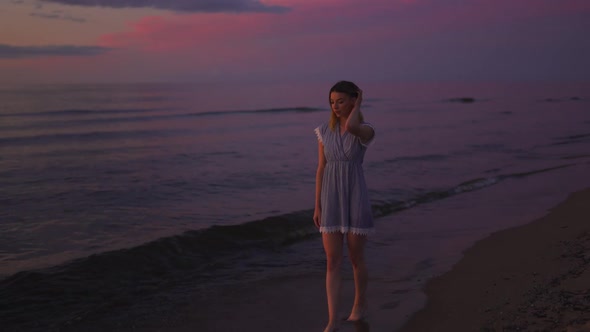 Beautiful Young Woman Walking at Sea on the Beach Enjoying Amazing Tender Sunset or Sunrise Wearing