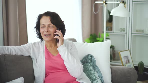 Mature Smiling Woman Talking Phone Sitting on Couch in Home Interior