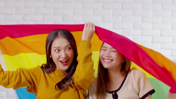 LGBTQ Asian lesbian young couple smiling holding pride flag happiness with love together