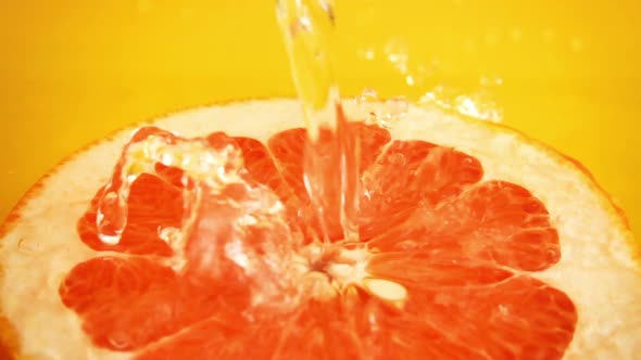 Half of a grapefruit in a jet of water on an orange background. Slow motion.