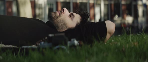 Man with beard lying down on the grass next to his camera rack-focus