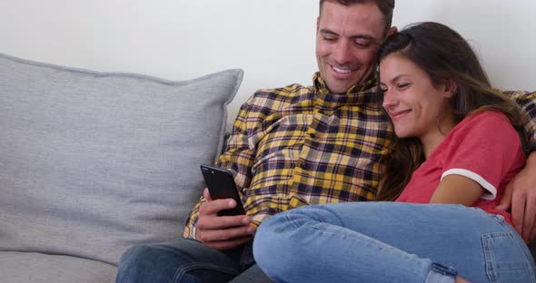 Cute couple using mobile phone in living room at home 