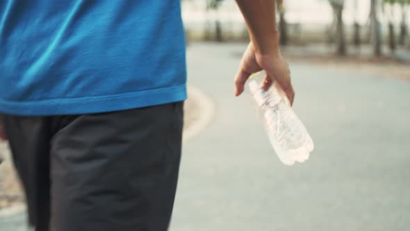 Young Asian man athlete walking and holding water bottle after running exercise at the park.