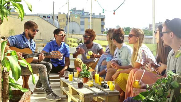 Cheerful friends sitting around table on rooftop and talking