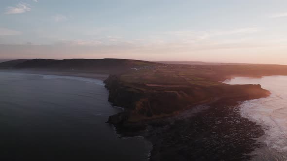 AERIAL: Dolly towards Rhossili peninsula during hazy sunrise, Gower, 4k Drone