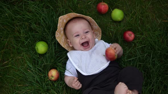 Happy Newborn Child in Summer Panama Hat Fall Down Laying on Grass Barefoot in Summer Sunny Day with