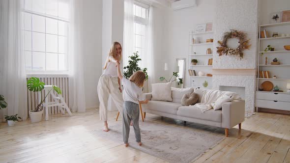 Young Blonde Mother Mom Dancing with Little Daughter Small Girl at Home Living Room Interior