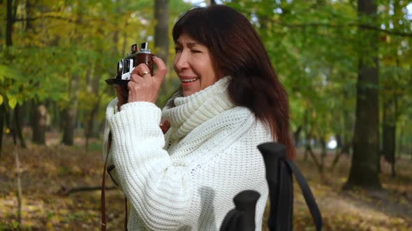 Side View Curios Talented Mature Woman Taking Photos with Camera Standing in Autumn Forest Outdoors