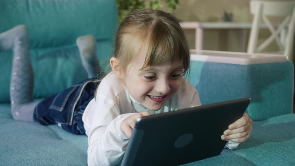 Adorable Kid Girl Using Digital Tablet Watching Cartoons Lying on Bed at Home.