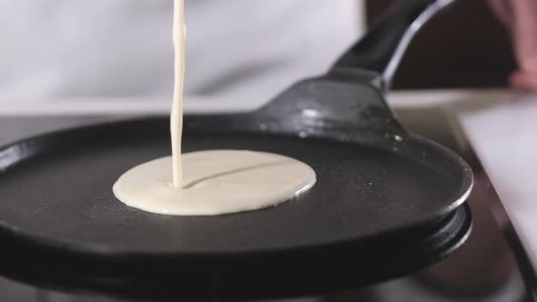 male cook prepares pancakes in hot pan.