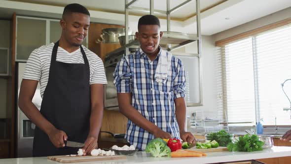 African american senior father and two adult sons standing in kitchen cooking dinner and talking