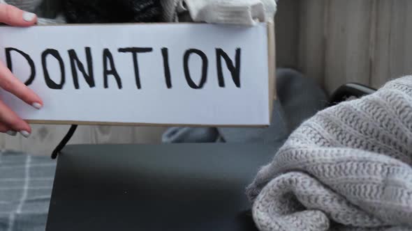 Female Volunteer Making Donation Box with Old Used Clothes Indoors