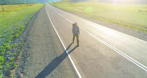 Flight Over Hitchhiker Tourist Walking on Asphalt Road. Huge Rural Valley at Summer Day