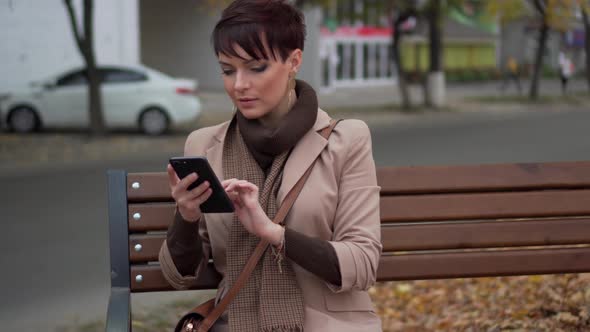 Young Female Uses Smartphone While Sitting on Bench