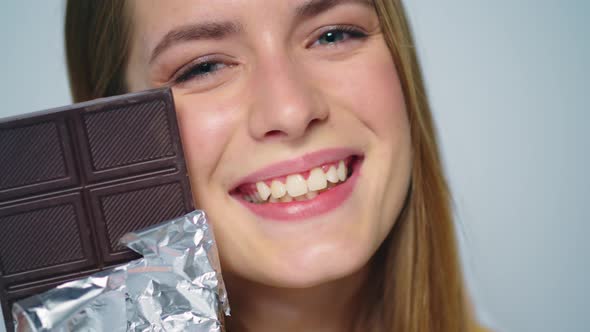 Closeup Young Woman Looking with Chocolate Bar at Camera Ion Grey Background