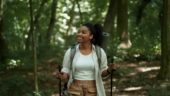 Young Happy Woman Tourist with Backpack Standing in Woodland with Walking Sticks Looking Around and