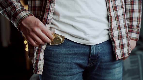 Caucasian Man Hand Closeup Takes Out Condom in Gold Package From Jeans Pocket