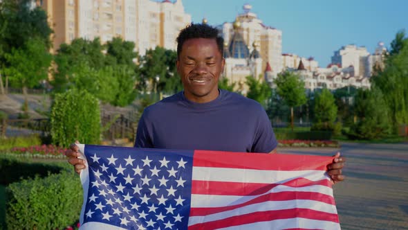 Portrait Afroamerican Man Holding an American Flag and Looks Camera in Summer