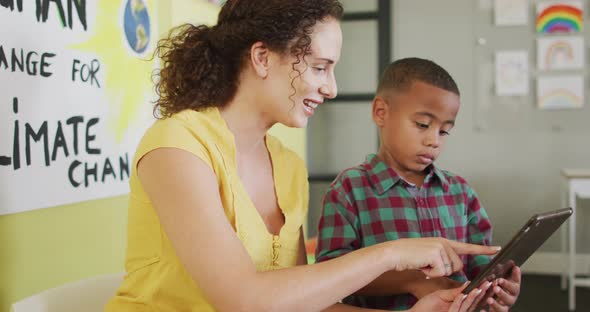 Video of happy caucasian female teacher and african american boy studying ecology in classroom alt