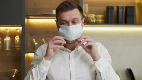 Young Man Puts Medical Mask on Face Looking Into Camera