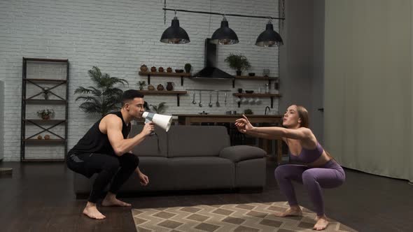 A Personal Trainer Yells Into a Megaphone Making the Girl Do Squats