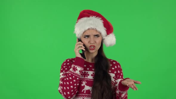 Portrait of Sweety Girl in Santa Claus Hat Is Angrily Talking for Mobile Phone. Green Screen