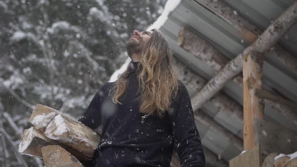 Brutal man holding firewood and admiring falling snowflakes