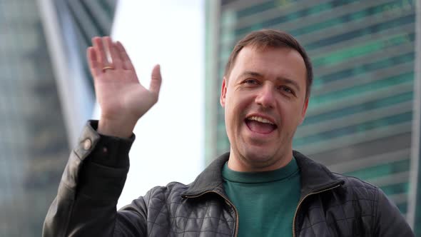 Millennial Guy Looking at Camera Smiling and Waving Hello Greeting Gesture Standing at City Street