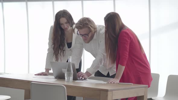 Handsome Blond Man in Glasses Bent Over Netbook in a Light Comfortable Office