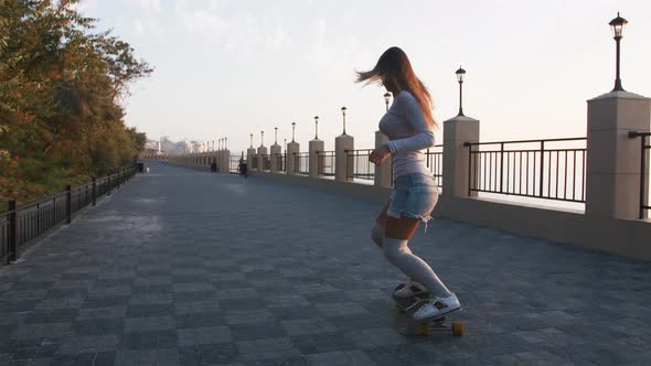 Young Stylish Attractive Woman Skateboarding at Sunrise on Seafront Slow Motion