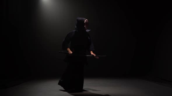 Kendo Fighter Performing Martial Art with Katana Sword at Dark Studio Under Spotlight.