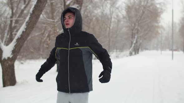 Young Guy in Jacket Jumps on the Spot and Stretches in Park Winter Front View