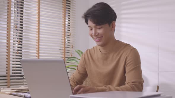 At home, a business asian man types and works online on a desk table with a laptop.