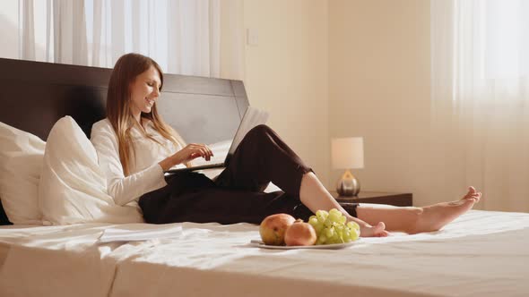 Attractive Young Woman Lying on Comfy Bed and Typing on Wireless Laptop