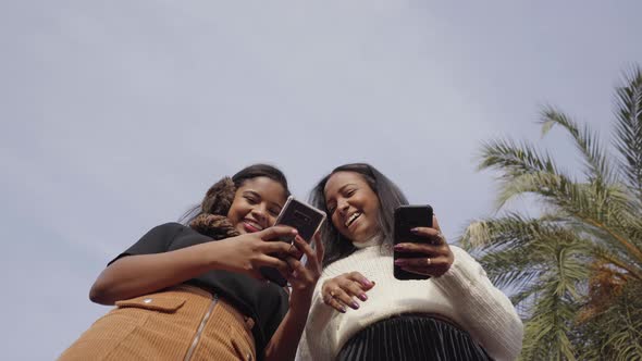 Low angle of two black girls using a mobile phone and laughing.