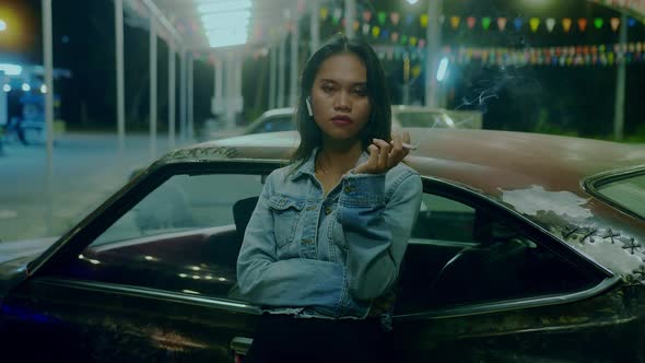 A Girl Smokes in Front of a Rusty Classic Car While Typing a Message Late at Night